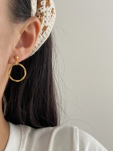 Close-up of a model wearing irregular gold geometric hoop earrings with a metallic finish
