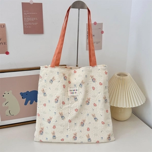 Detail of beige canvas bag with rabbit pattern, orange handles, and woven logo tag