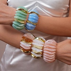 Stacked wavy acrylic bracelets with metallic accents worn by a model in satin dress