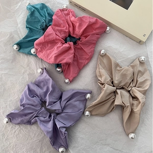 Flat lay of colorful fabric scrunchies with faux pearl edges on white paper background