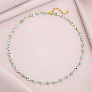 Detail of gold chain necklace featuring small evil eye charms on pink fabric background