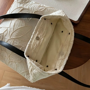 Detailed macro view of 3D leaf embroidery and premium leather straps on canvas tote bag
