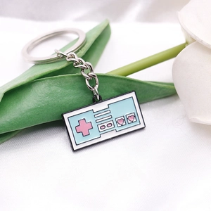 Close-up of a blue gamepad enamel keychain with pink hearts on white satin fabric