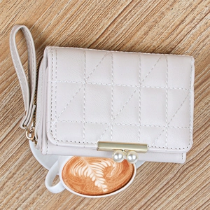 Detail of off-white quilted wallet featuring gold pearl clasp on wooden table