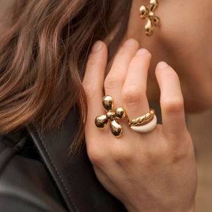 Close-up of golden flower ring and braided metal ring with beige resin band on model