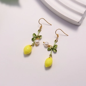 Macro detail of lemon pendant earrings with yellow fruit, green leaf, and white pearl