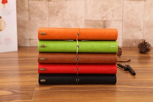 Detailed stack of five colorful leather notebooks with vintage metal charm elastic bands