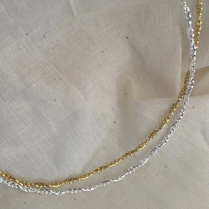 Close-up of minimalist faceted silver and gold bead necklaces on beige linen fabric