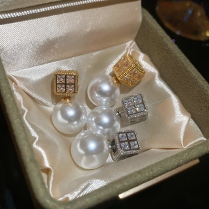 Detailed shot of luxury square zircon and white pearl earrings on champagne silk fabric