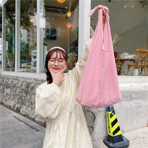Pink cotton linen tote bag with knot shoulder strap details shown in a lifestyle street setting