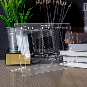 Close-up of a clear acrylic weekly planner board on a desk with metal stands