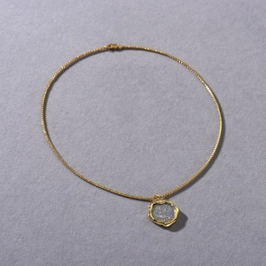 Detail of 18k gold plated necklace with irregular lucky coin pendant on dark grey texture