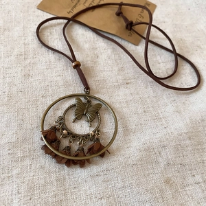 Detail of vintage bronze butterfly pendant with brown fringe flower on suede cord