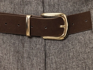Close-up of deep brown suede belt with oval gold buckle on grey wool trousers