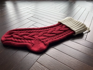 Close-up of red cable knit Christmas stocking with white folded cuff on wooden floor