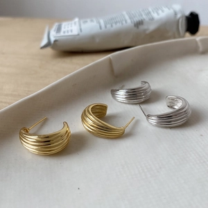 Macro shot of minimalist C-shape ribbed earrings in gold and silver on a ceramic tray
