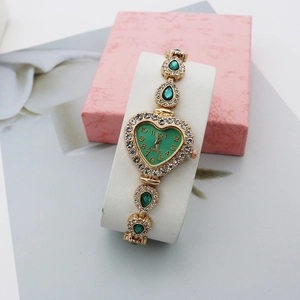 Détail de montre cœur vert avec lunette en strass et pierres poires sur bracelet doré