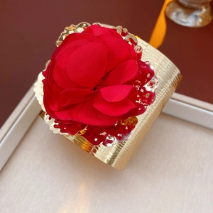 Détail d'une fleur en tissu rouge sur un bracelet jonc doré texturé dans un plateau