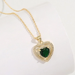 Golden emerald heart necklace with zircon crystals on a minimalist white platform