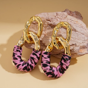 Detail of pink zebra print leather and gold geometric oval earrings on a stone