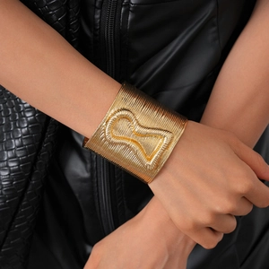 Macro view of wide gold metal cuff bracelet with linear texture and hourglass detail