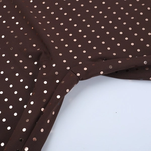Close-up of brown halter jumpsuit fabric with gold glitter polka dots and seam details