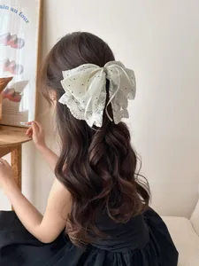 Macro view of cream lace bow hair claw with embroidery and polka dots on wavy hair