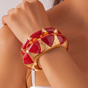 Detail view of a wide gold metal cuff bracelet with red 3D triangular enamel patterns