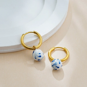 Close-up of 18K gold hoop earrings with blue and white porcelain enamel cloud pendants