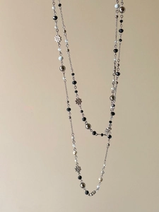 Detail of beaded necklace with black beads, white marble beads and silver flower pendant