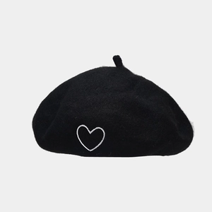 Detailed close-up of a black wool beret featuring a white heart embroidery on a flat surface
