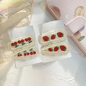Detailed close-up of handmade embroidered cherry and strawberry hair clips on lace