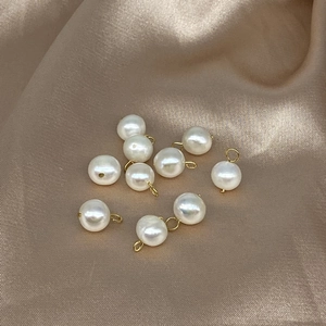 Detail of nine white near-round pearls with gold loops on soft beige silk fabric