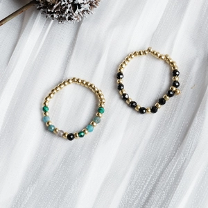 Macro shot of handmade beaded rings with gold accents and natural stones on white silk