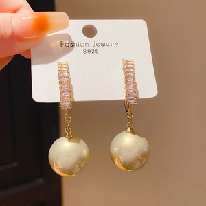 Détail de boucles d'oreilles dorées élégantes avec strass brillants et perles blanches