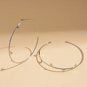 Detail of silver geometric hoop earrings with spiked rivets on a warm background
