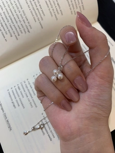 Macro detail of three-pearl zircon pendant on a silver-tone chain held over a book