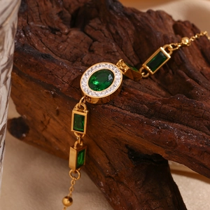 Detail of 18K gold plated bracelet with emerald green stones on textured wood