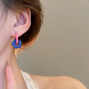 Detail of pink hoop earrings with a blue flower pendant worn by a female model