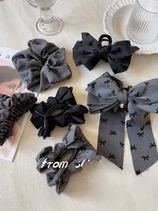 Dettaglio di fermagli e scrunchie grigi con motivi a fiocco nero e un ciondolo d'argento
