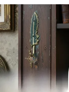 Gancio da parete a forma di piuma in bronzo con vecchia chiave su fondo di legno rustico