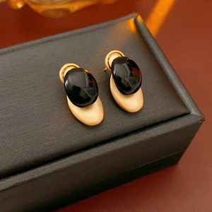 Detail of matte gold and black onyx-style stud earrings on a textured jewelry box