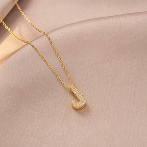 Macro detail of gold-plated letter J pendant featuring micro-pave cubic zirconia on silk