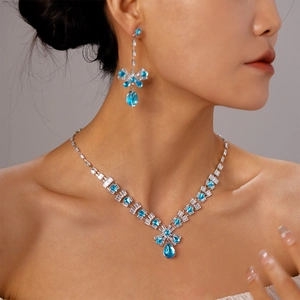 Close-up of a silver bow necklace and earrings set with blue teardrop zircon stones
