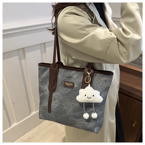 Detail of grey tote bag with brown handles and a plush white cloud charm on shoulder