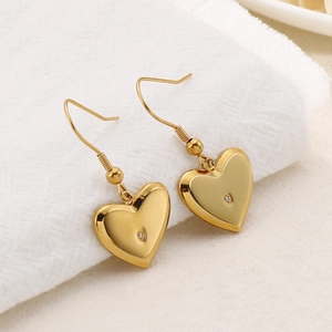 Golden heart-shaped hook earrings with small central rhinestone on white linen background
