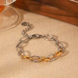Close-up of mixed gold and silver link bracelet with textured finish on beige fabric