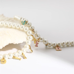 Close-up of pearl bracelet with gold and colorful enamel Sofia letter pendants on shell