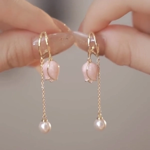 Elegant gold tulip earrings with long tassels and pearls shown held in hand