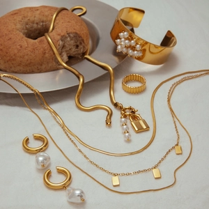 Parure de bijoux dorés avec collier de perles, chaîne serpent et bague large sur tissu blanc